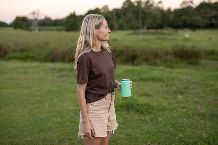 Mint green insulated coffee cup with blue lid, held in hand outdoors in field setting