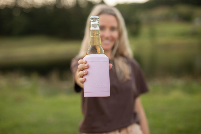 Dusty pink neoprene bottle cooler holding a beer bottle, displayed outdoors