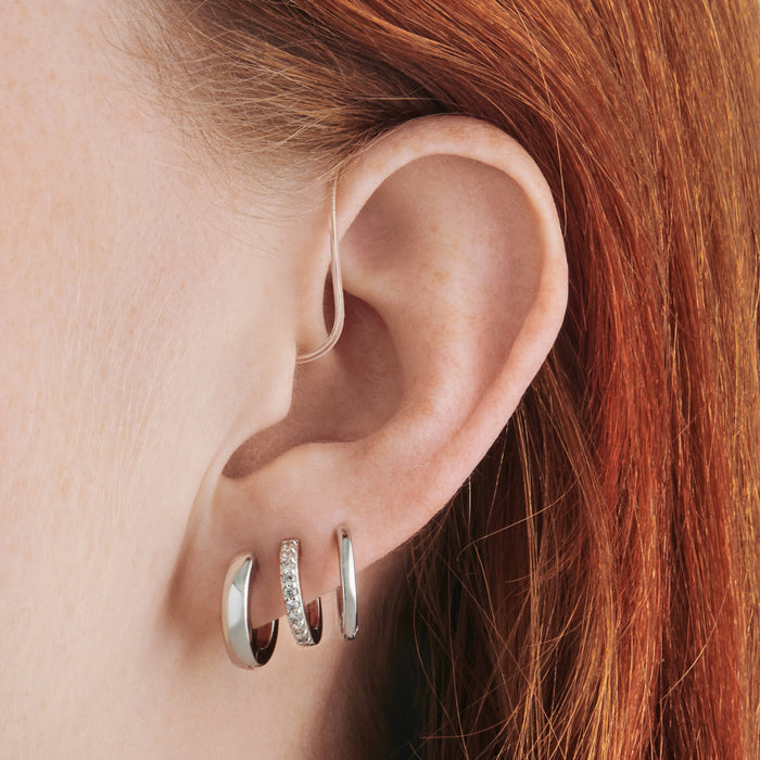 a set consisting of a pair of silver mini chunky huggies, silver mini pave huggies, and silver small slim huggies on ear [hover] color:null|silver