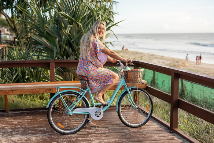 Hooded towel in coral geometric print worn as dress on woman riding turquoise bike on beach boardwalk