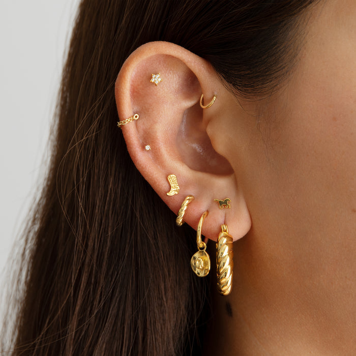 A small gold huggie with a cowboy hat charm on an ear. [hover] color:null|gold