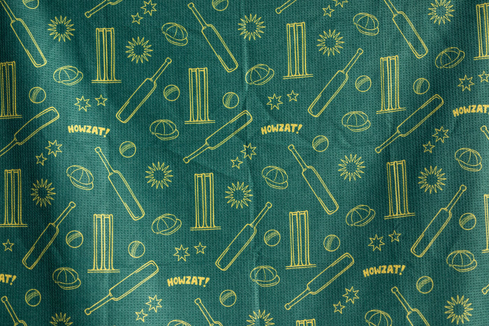 Teal beach towel with gold cricket-themed pattern including bats, stumps, balls, planets, stars, and HOWZAT! text