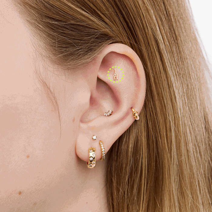Close up of gold cat shaped earrings on an ear on a neutral background