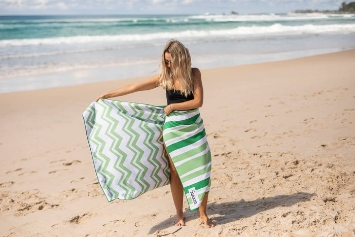 Green and white chevron recycled beach towel with striped wrap, displayed on sandy beach
