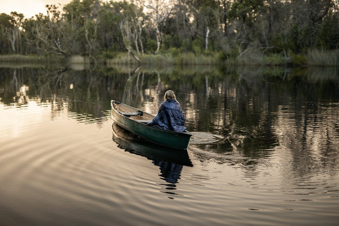 Image of a woman wrapped in Nakie's Deep Ocean Blue Sustainable Down Puffy Blanket while on a boat