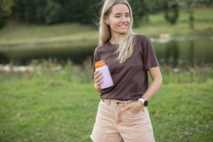 Dusty pink insulated coffee cup with orange lid, held by woman wearing brown t-shirt outdoors