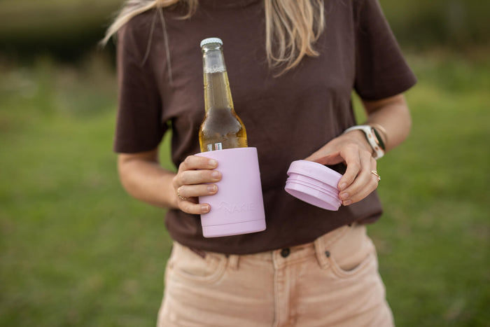 Dusty pink insulated coffee cup with matching lid, held by person carrying beer bottle outdoors