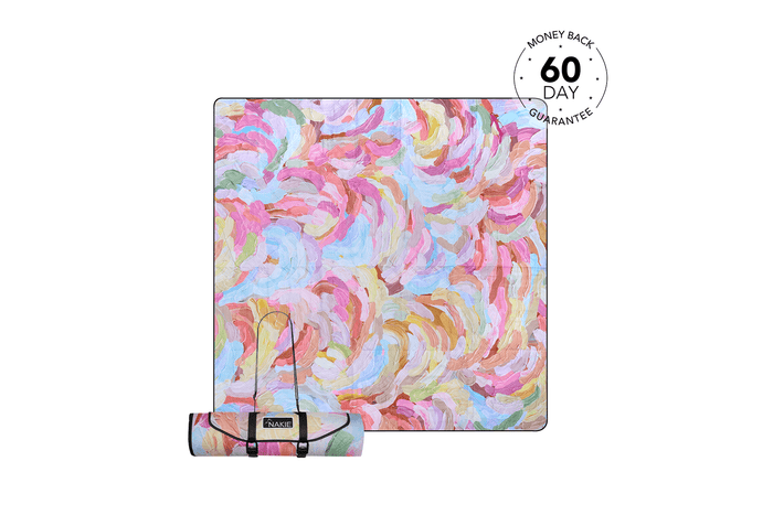 Colorful abstract swirl picnic blanket in pink, blue, yellow, and green with carrying strap rolled up below.