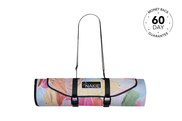 Rolled picnic blanket with multicolored floral print, black straps, and Nakie logo label, front view.
