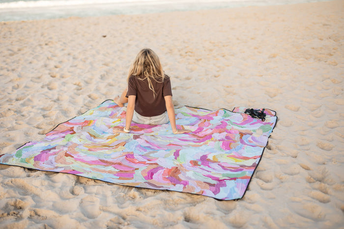 Recycled picnic blanket with vibrant multicolor swirl abstract pattern, displayed on beach sand.