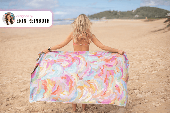 Recycled sand-free beach towel with multicolor abstract brushstroke pattern, held open on beach