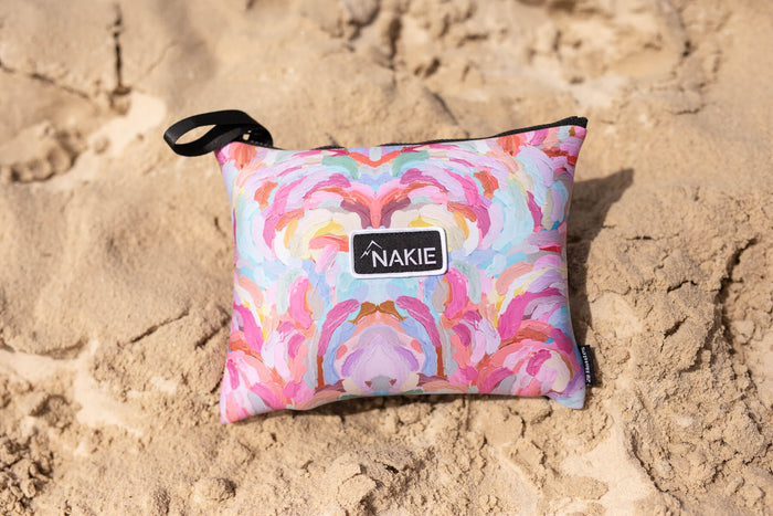 Colorful geometric patterned beach towel in pink, orange, yellow and blue with black handle strap on sand.