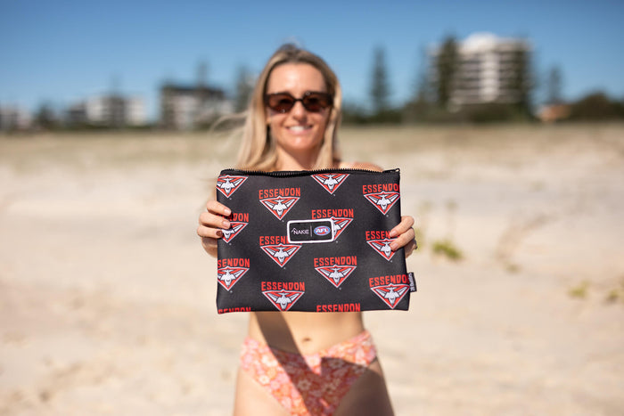 Black Essendon Bombers AFL recycled sand-free beach towel with red and white logo pattern, held at beach