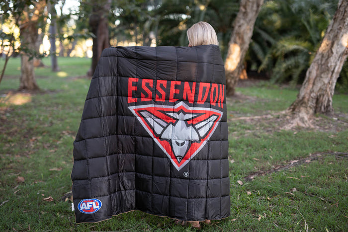 Black quilted puffy blanket with Essendon Bombers red and white logo and AFL badge, displayed on person outdoors.
