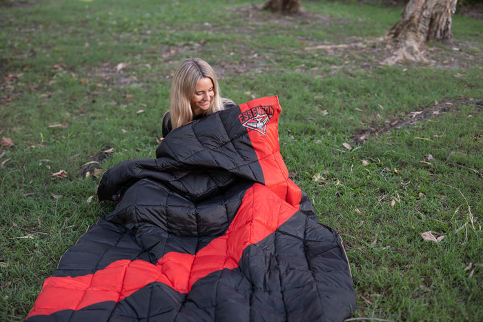 Red and black Essendon Bombers puffy blanket with quilted down fill, displayed outdoors on grass.