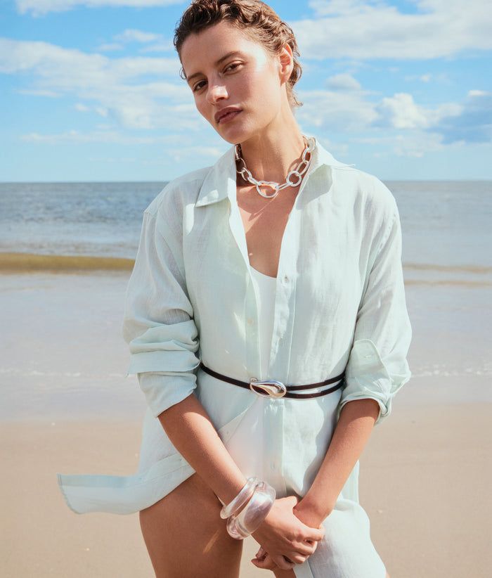 Model on beach wears aqua shirt with Estelle Belt in Silver, Porto Chain in Silver and clear resin cuffs