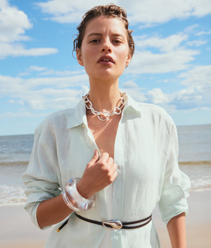 Model on beach, alt view, wearing aqua shirt with Estelle Belt in Silver, Porto Chain in Silver and clear resin cuffs