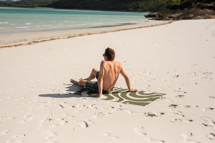 Eucalyptus green wave-patterned beach towel with recycled material, displayed on sand at tropical beach