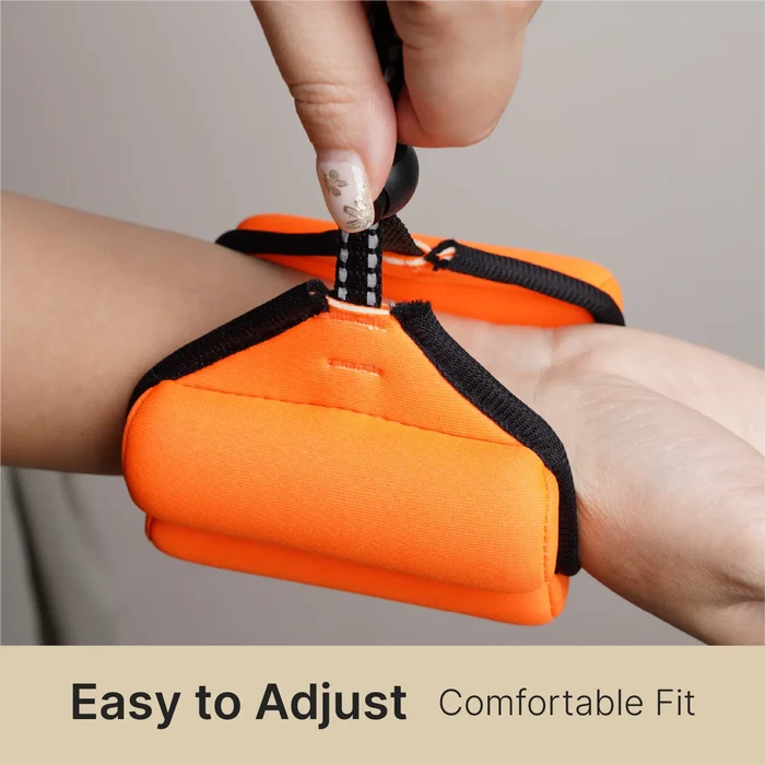 A hand with painted nails secures a black strap on a bright orange Catalyst Case US Floating Wrist Lanyard around anotherÃƒÂ¢Ã¢â€šÂ¬Ã¢â€žÂ¢s wrist. Neutral background. Text below: "Easy to Adjust Comfortable Fit.
