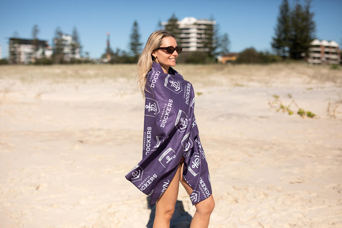 Fremantle Dockers purple beach towel with white logo pattern, worn draped around woman on sand