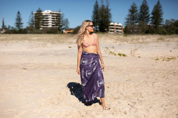 Navy beach towel with white Fremantle Dockers AFL logo print, worn as sarong on sandy beach