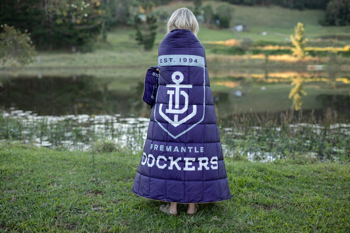 Navy Fremantle Dockers puffy blanket with anchor logo and "EST. 1994" text, worn as a cape outdoors.