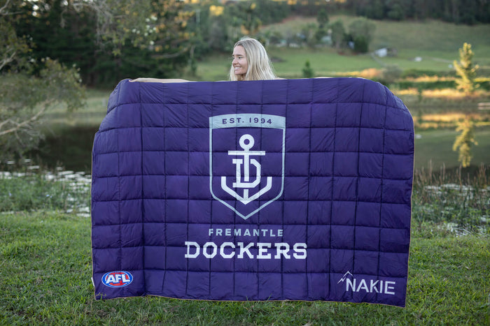 Navy quilted puffy blanket featuring Fremantle Dockers anchor logo, "EST. 1994" text, and Nakie branding, displayed outdoors