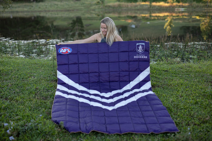 Fremantle Dockers AFL purple quilted blanket with white chevron stripe and team logos, held outdoors.