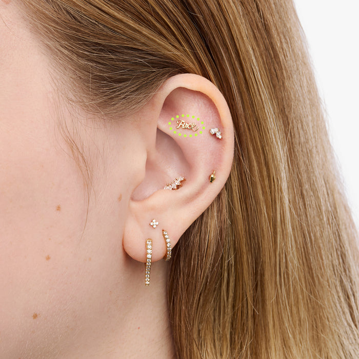 Close-up of an ear with multiple gold earrings on a neutral background