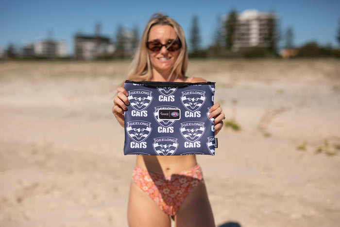 Geelong Cats navy beach towel with repeated logo pattern, held up on sandy beach