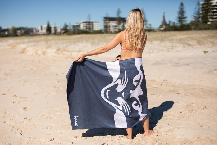 Navy and white Geelong Cats AFL beach towel with graphic design, displayed on sand at beach.