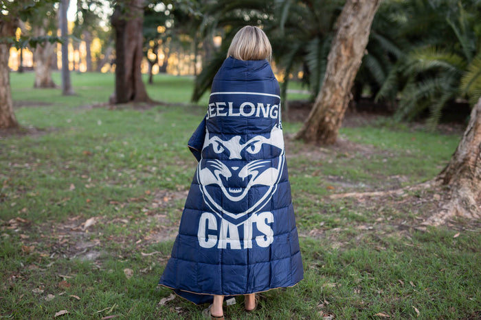 Navy Geelong Cats puffy blanket with white logo and text, worn as a wrap by person outdoors.