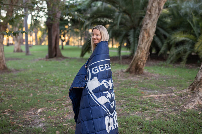 Navy Geelong Cats AFL puffy blanket with white logo and stripes, draped over woman's shoulders outdoors.