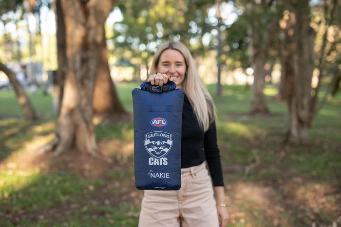 Navy Geelong Cats AFL dry bag with roll-top closure and team logo, held open by person outdoors.