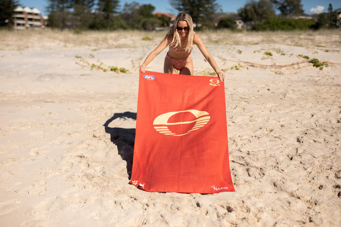 Gold Coast SUNS recycled sand-free beach towel in red with cream logo, displayed on beach.