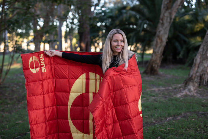 Red quilted puffy blanket with Gold Coast Suns AFL logo and gold cross design, displayed outdoors.
