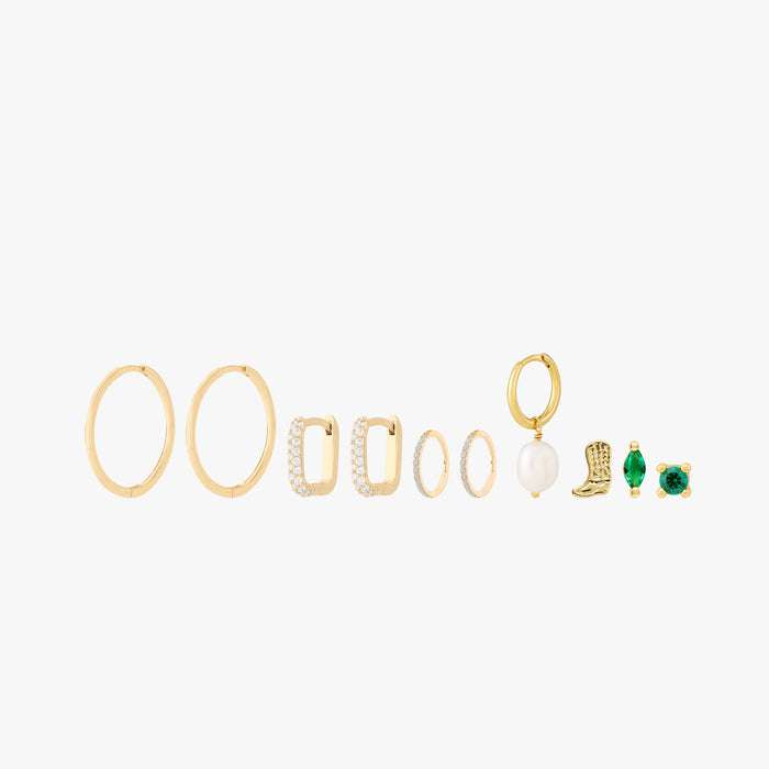 This image shows a set of 14k Yellow Gold plated earrings. The set includes one thin hoop pair, two pairs of huggies. One square shaped with clear cz stones and another with pearl cz stones. There is a singular open pearl huggie and three singular studs. There is a cowboy boot, a marquise with a green cz stone and a green cz stone stud flatback.