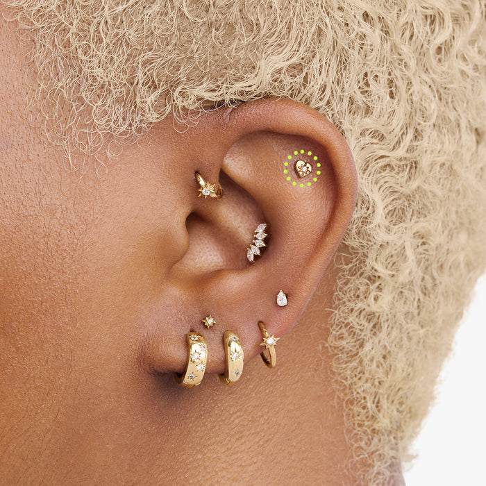This is an image of a gold-toned titanium flatback stud in the shape of a heart with a twinkle shaped star within it, and a crystal CZ within that circled on an ear.