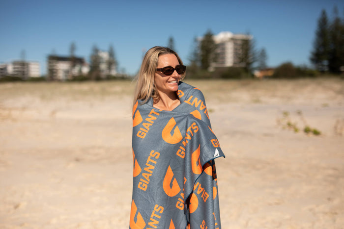 GWS Giants recycled sand-free beach towel in grey and orange with repeating logo pattern, draped on person at beach