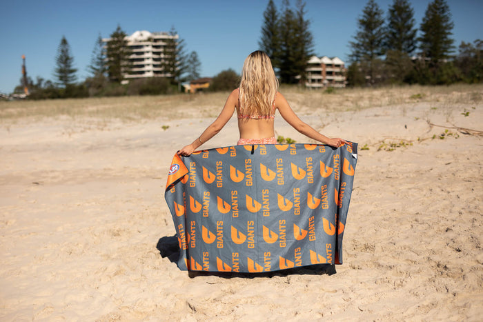 GWS Giants grey beach towel with orange logo pattern, held open on sand beach