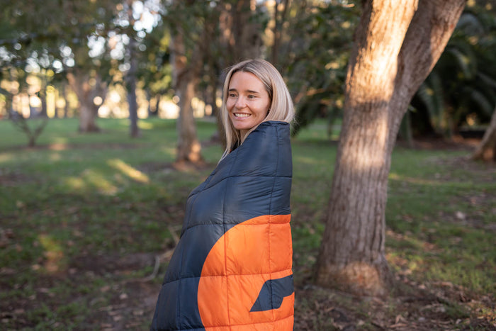 Navy and orange color-block quilted puffy blanket wrapped around person outdoors