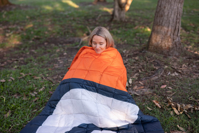 Orange, navy and white quilted puffy blanket draped over person sitting outdoors