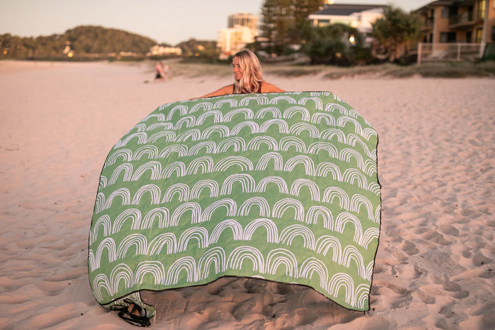 Green and white geometric arc patterned recycled picnic blanket displayed on beach sand