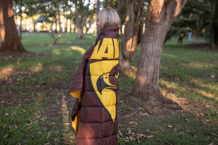Burgundy and gold patterned sustainable down puffy blanket worn as a wrap, showing Hawthorn Hawks AFL design on back view.