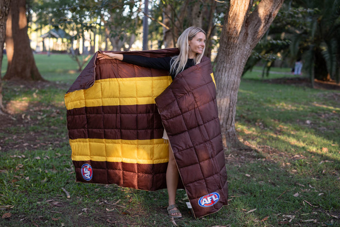 Brown and gold striped quilted puffy blanket with AFL Hawthorn Hawks logo, displayed draped around person outdoors.