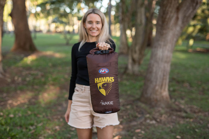 Brown Hawks AFL puffy blanket with roll-top closure and logo, held up by woman outdoors