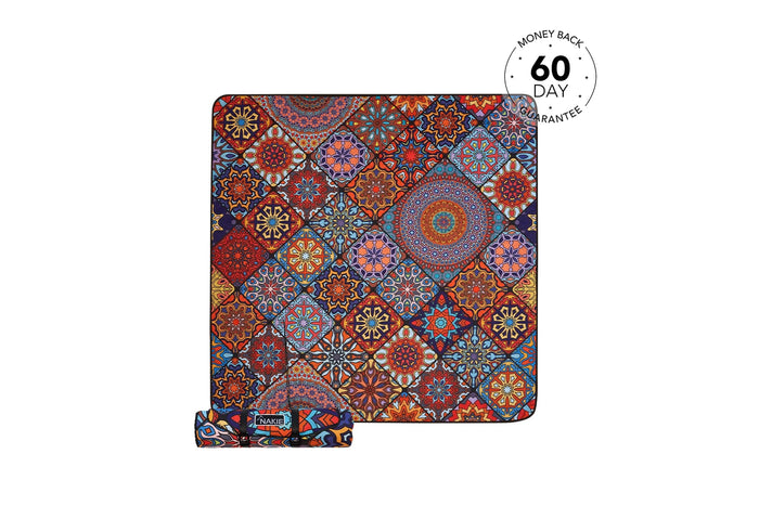 Recycled picnic blanket with multicolored ornamental tile pattern in red, blue, orange and gold, rolled with carrying strap.