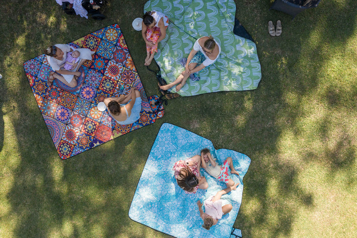 Recycled picnic blankets in blue, green, and red geometric patterns displayed on grass during outdoor family gathering.