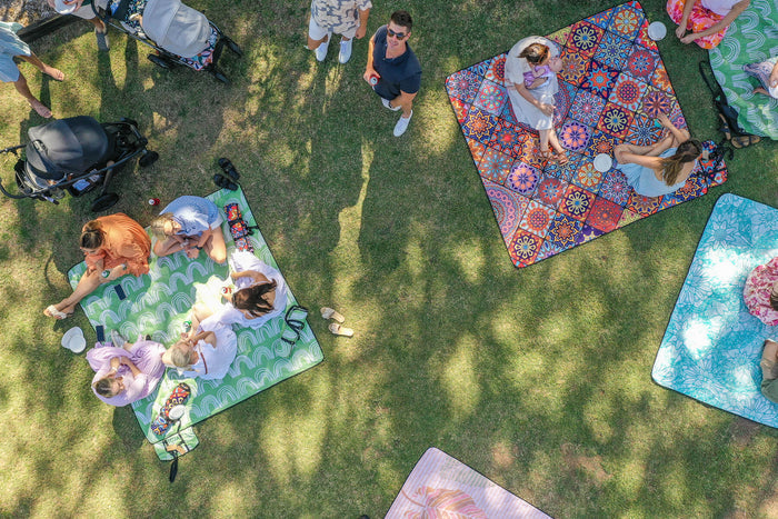 Overhead view of colorful patterned picnic blankets spread on grass with families relaxing during outdoor gathering
