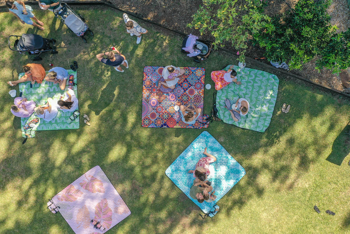 Recycled picnic blankets with colorful patterns in use on grass during outdoor family gathering overhead view